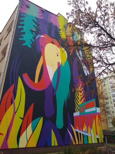 Ten kolorowy mural został namalowany w Warszawie na Woli, w pobliżu stacji Metra, i jest częścią projektu artystycznego mającego na celu ożywienie przestrzeni miejskiej oraz nawiązanie do lokalnej historii i kultury.